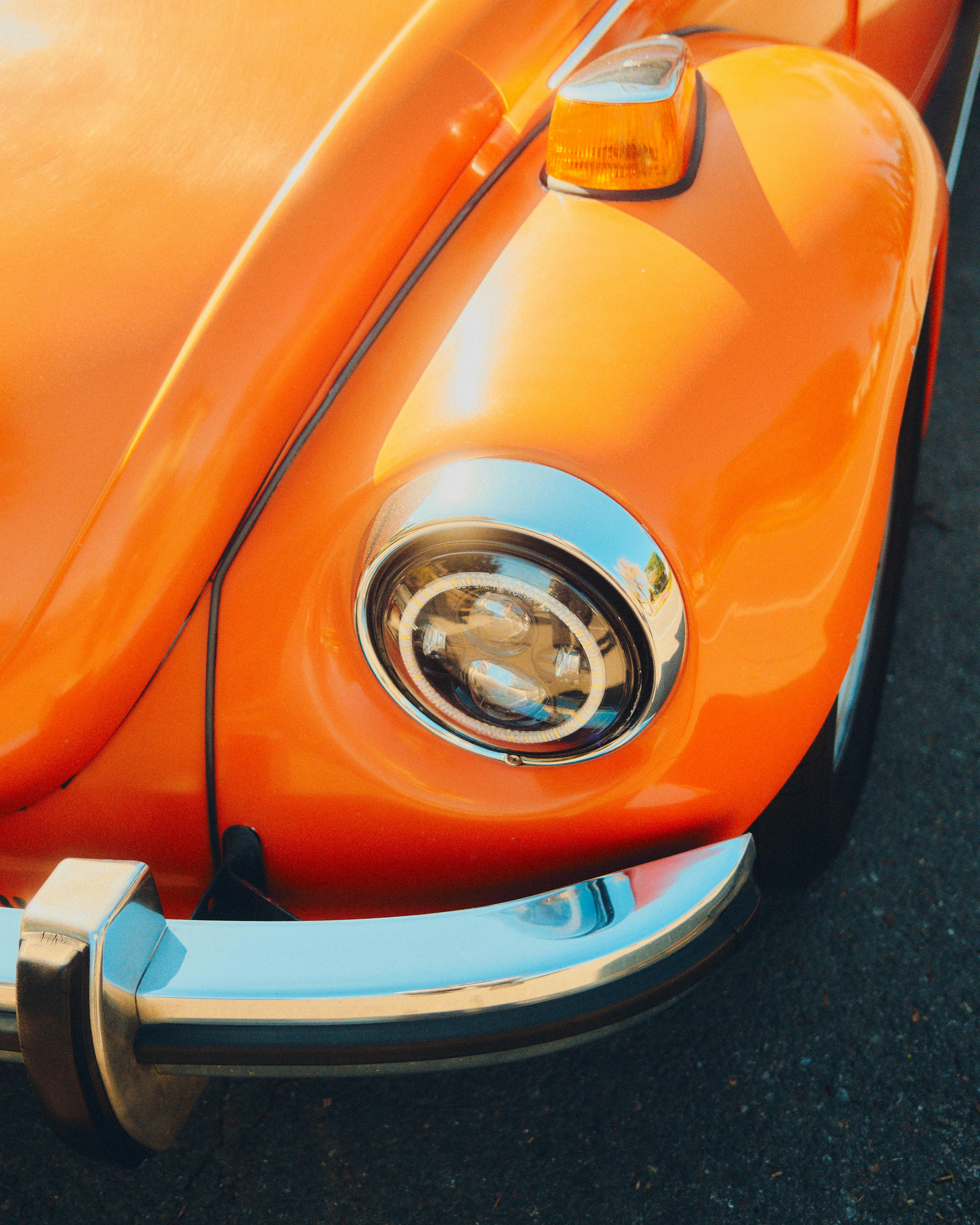 Close-up of a vibrant orange classic Volkswagen Beetle, highlighting its headlight and bumper details.