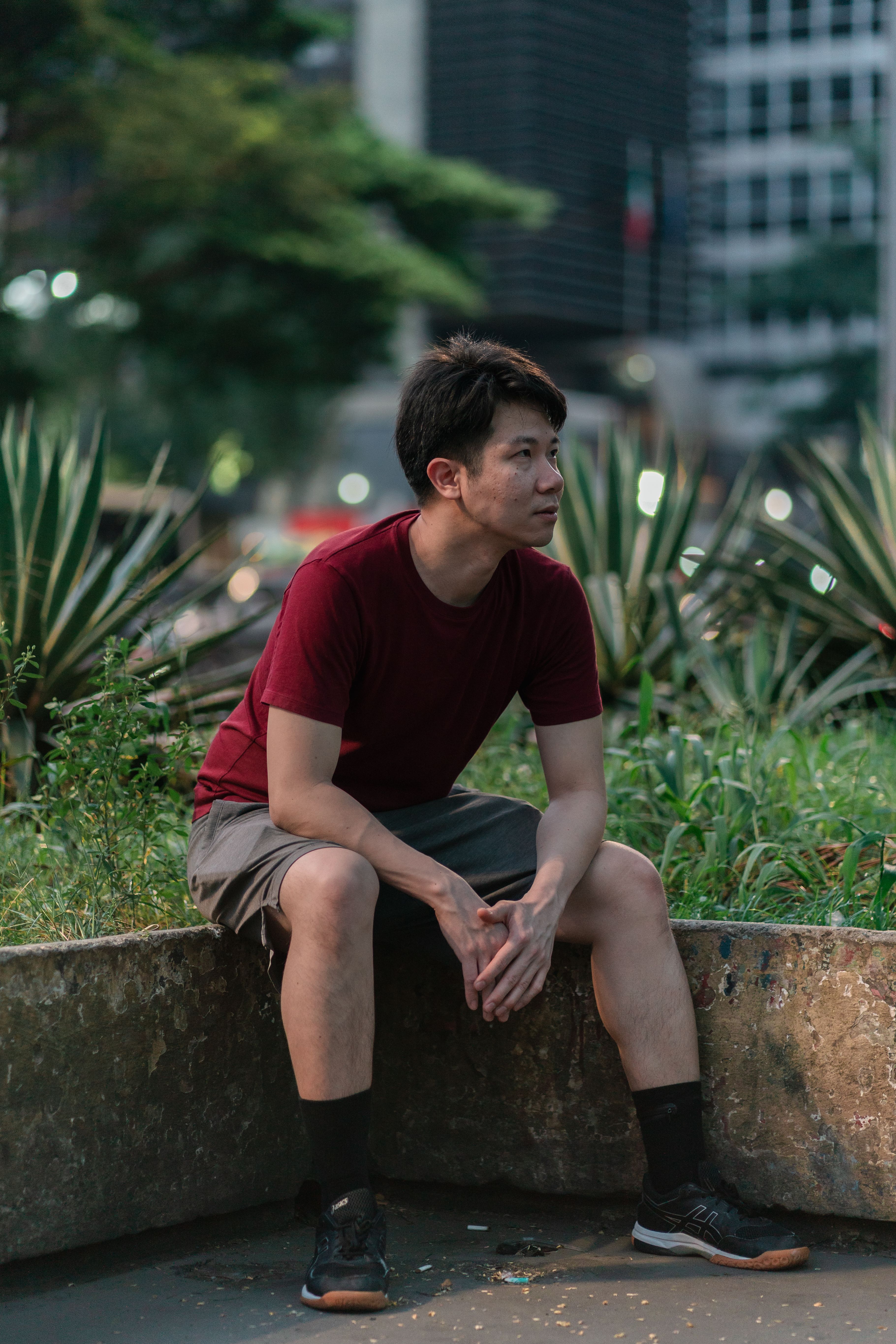 Young man in a casual outfit sitting in a city park during the day.