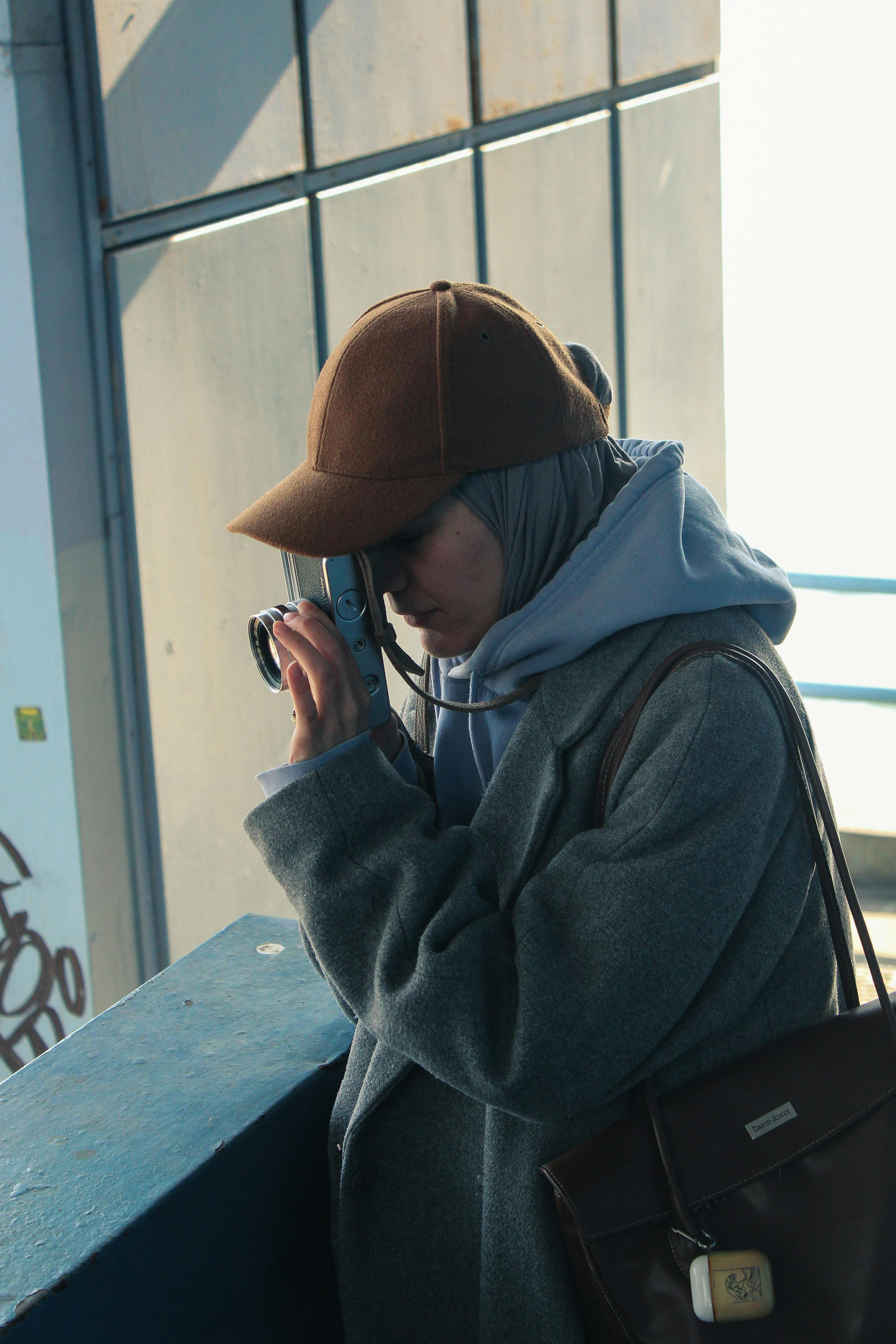 Zadarmo Bočný pohľad na ženu v hidžábe a čiapke, ktorá fotografuje vonku. Fotka z fotobanky