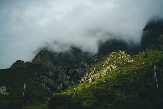 Misty clouds envelop rugged mountains, creating a dramatic natural scene.