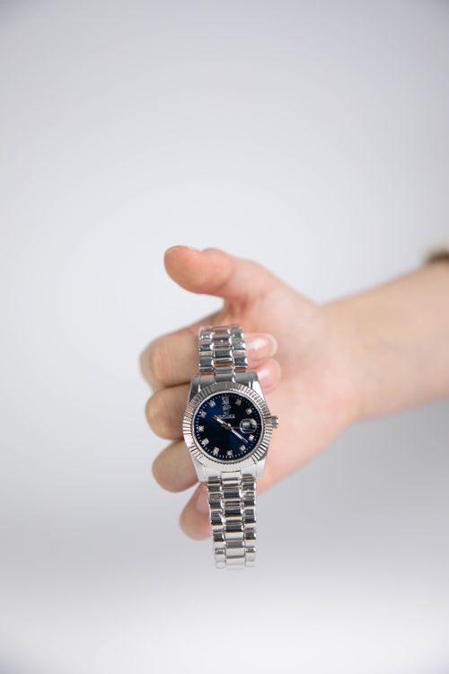 Free Close-up of a silver wristwatch with a black dial held in a hand against a neutral background. Stock Photo