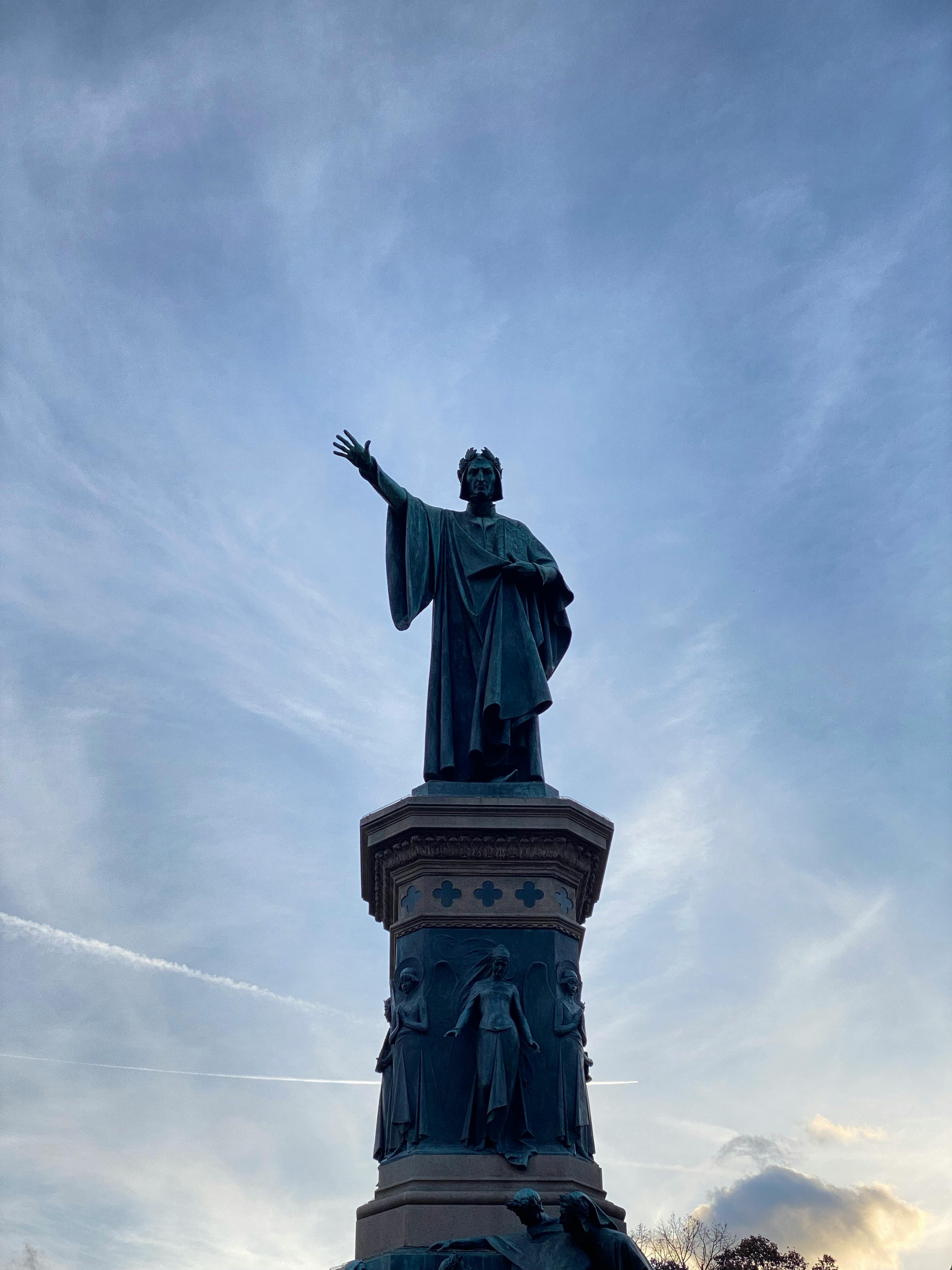 Statue of Dante Alighieri against a dramatic sky in Trento, Italy, symbolizing art and patriotism.
