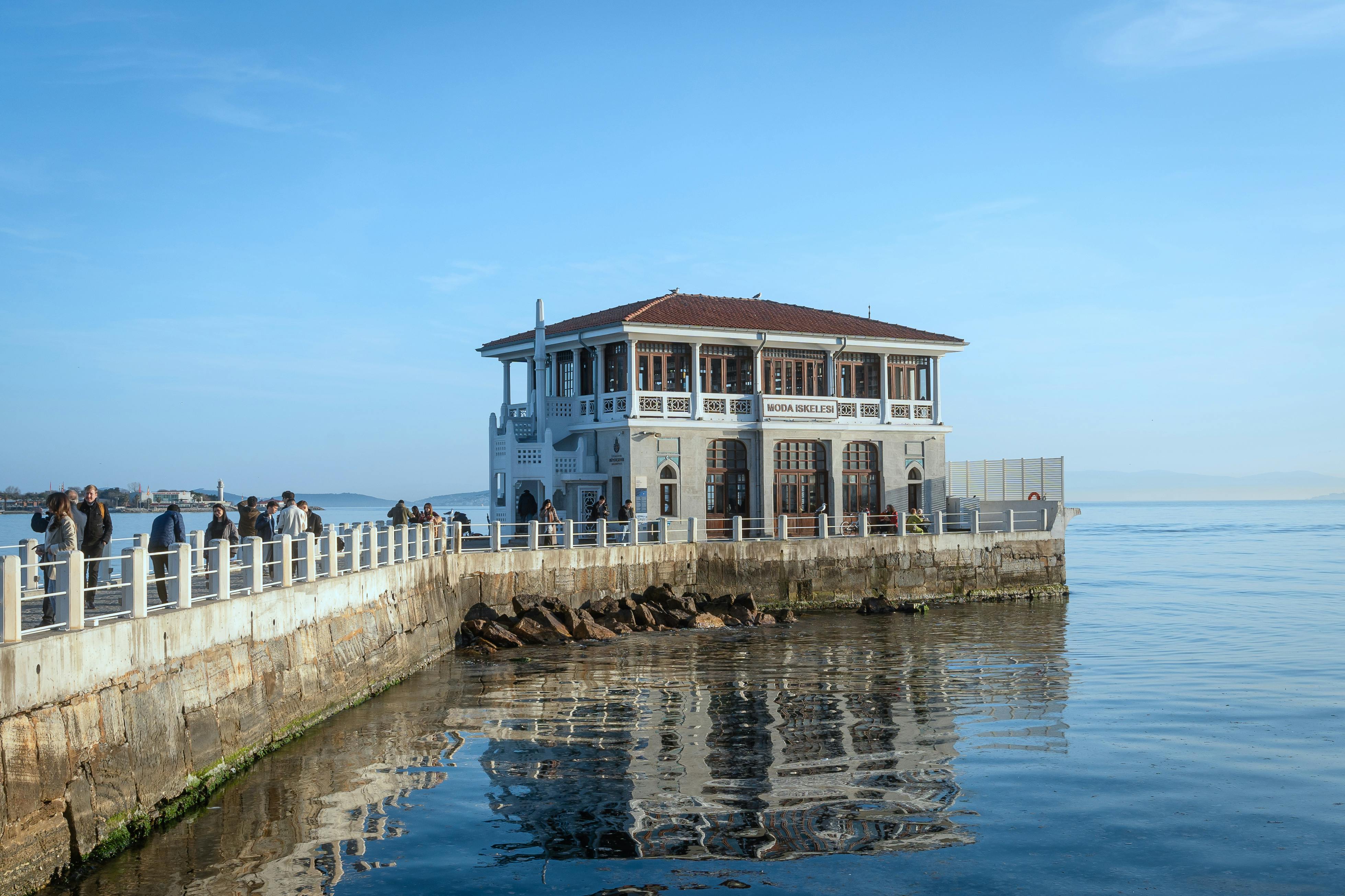 Gratis Naturskjønn utsikt over Moda Pier med en klassisk bygning og folk som nyter vannkanten. Arkivbilde