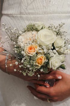 Close-up of a bride holding a beautiful bouquet of white and peach roses.