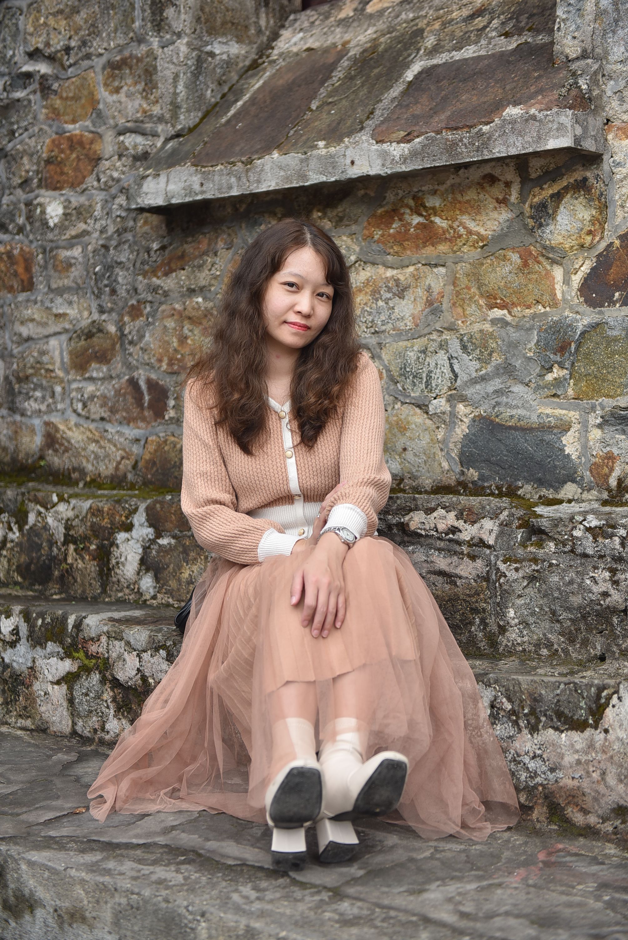 Young Woman in Peach Dress Sits by Stone Wall  Free Stock Photo