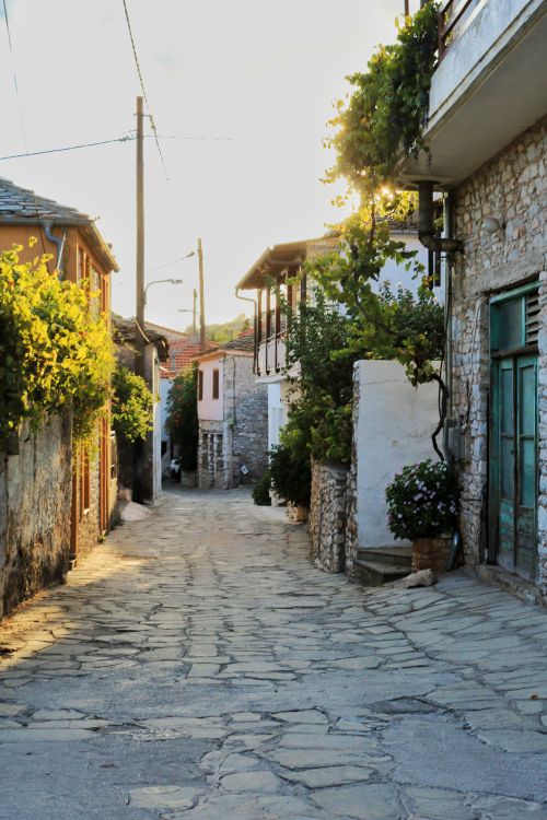 Free A quaint rustic stone-paved street with charming houses at sunset, offering a serene village ambiance. Stock Photo