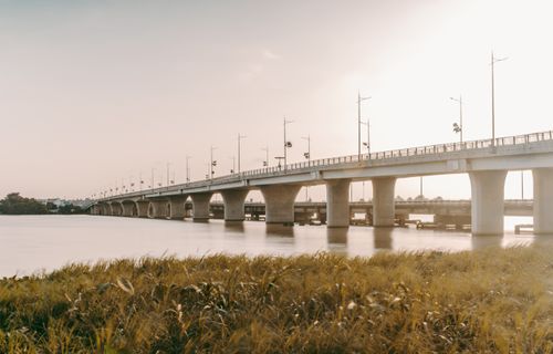 Free Peaceful view of a long bridge extending over a serene river with sunset lighting. Stock Photo