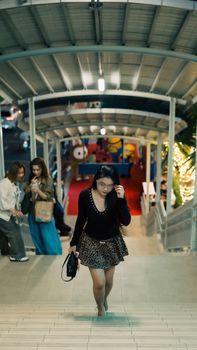 A woman in a stylish outfit ascends an illuminated staircase in a lively urban setting.