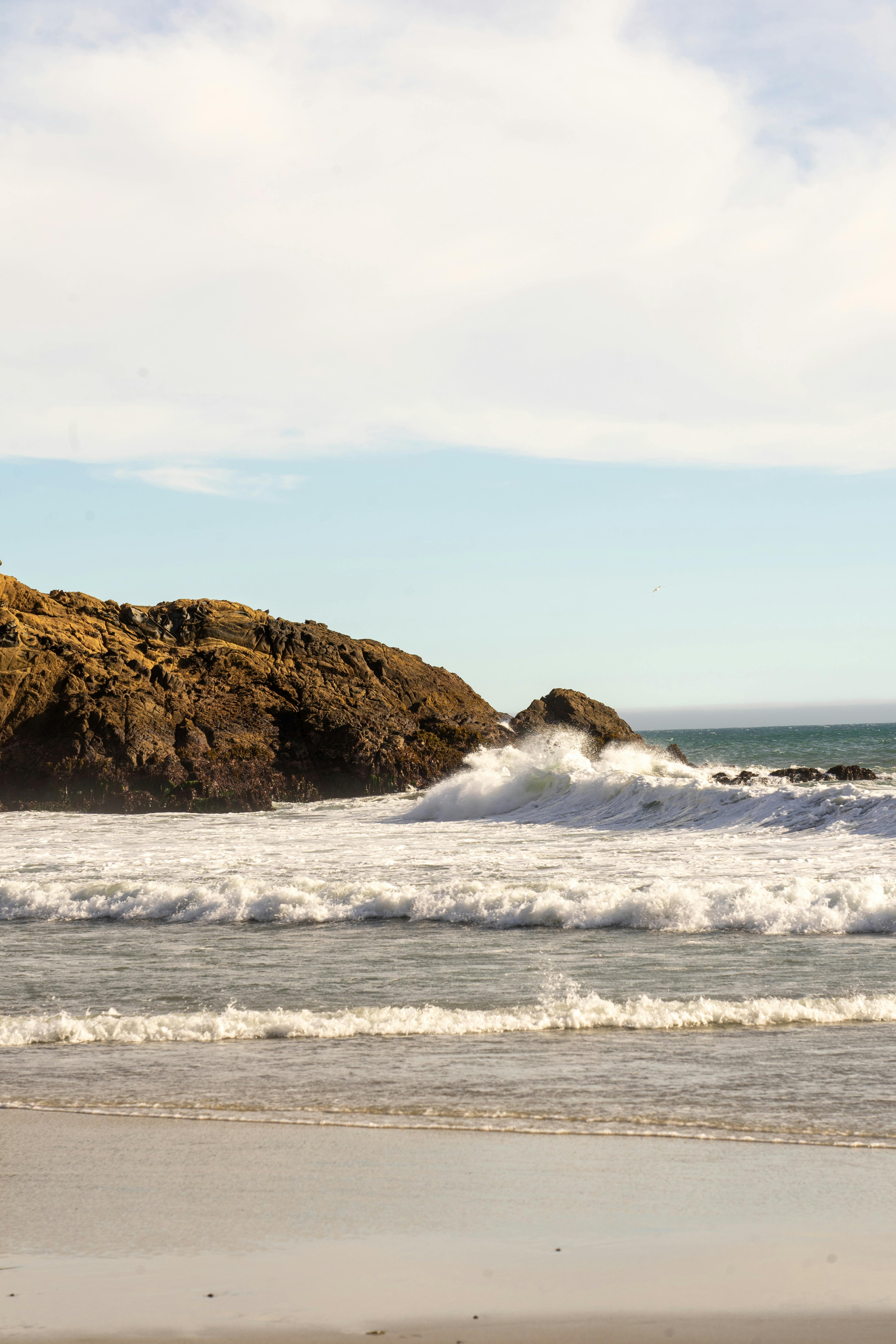 Peaceful scene of waves crashing against rocky shore under clear skies in California, USA.