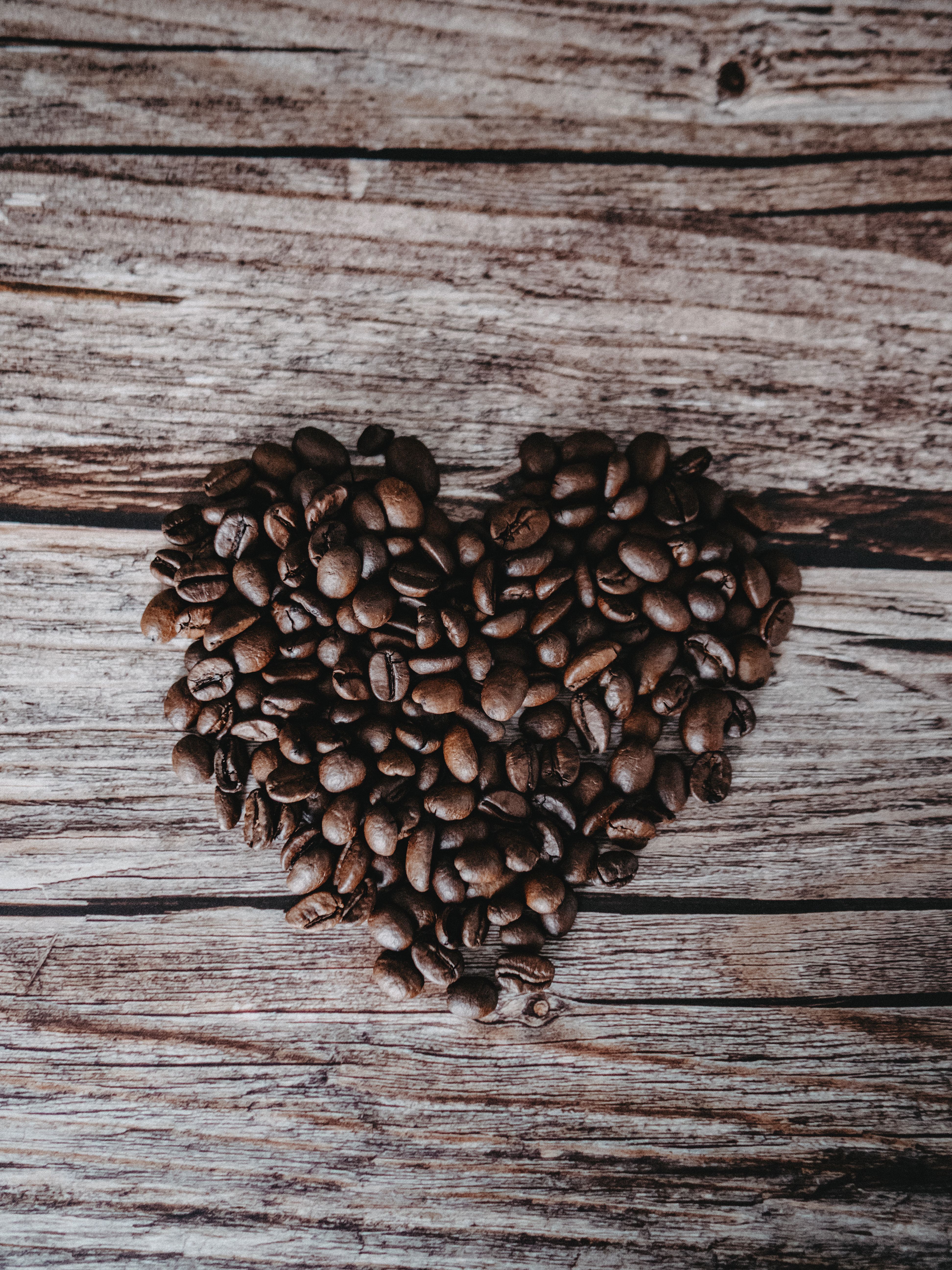 Heart made of coffee beans on rustic wooden surface, perfect for coffee lovers.