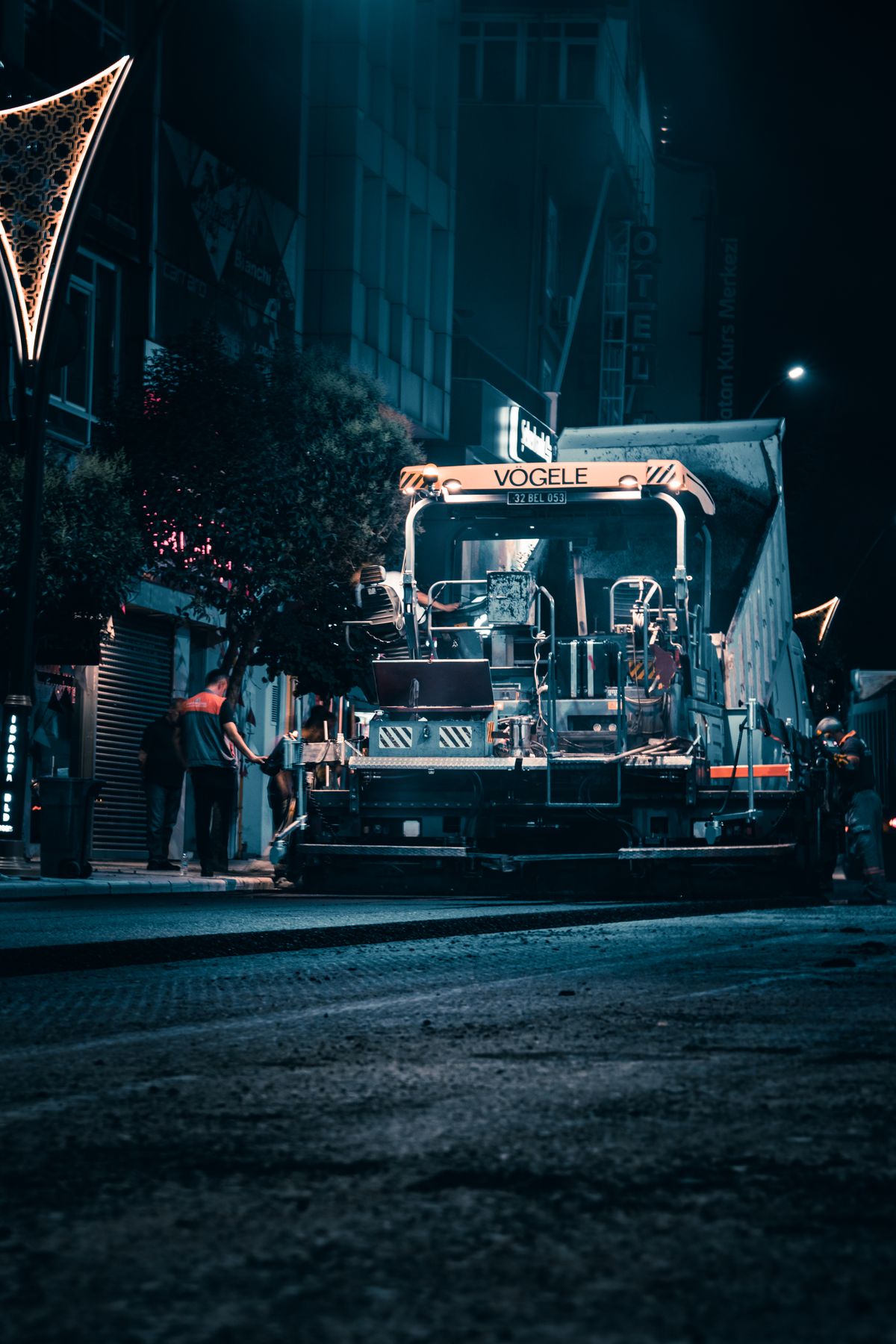 Night road construction with illuminated machinery working on an urban street resurfacing job
