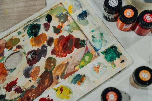Top view of a colorful artist's palette with various poster paints arranged for creative work.