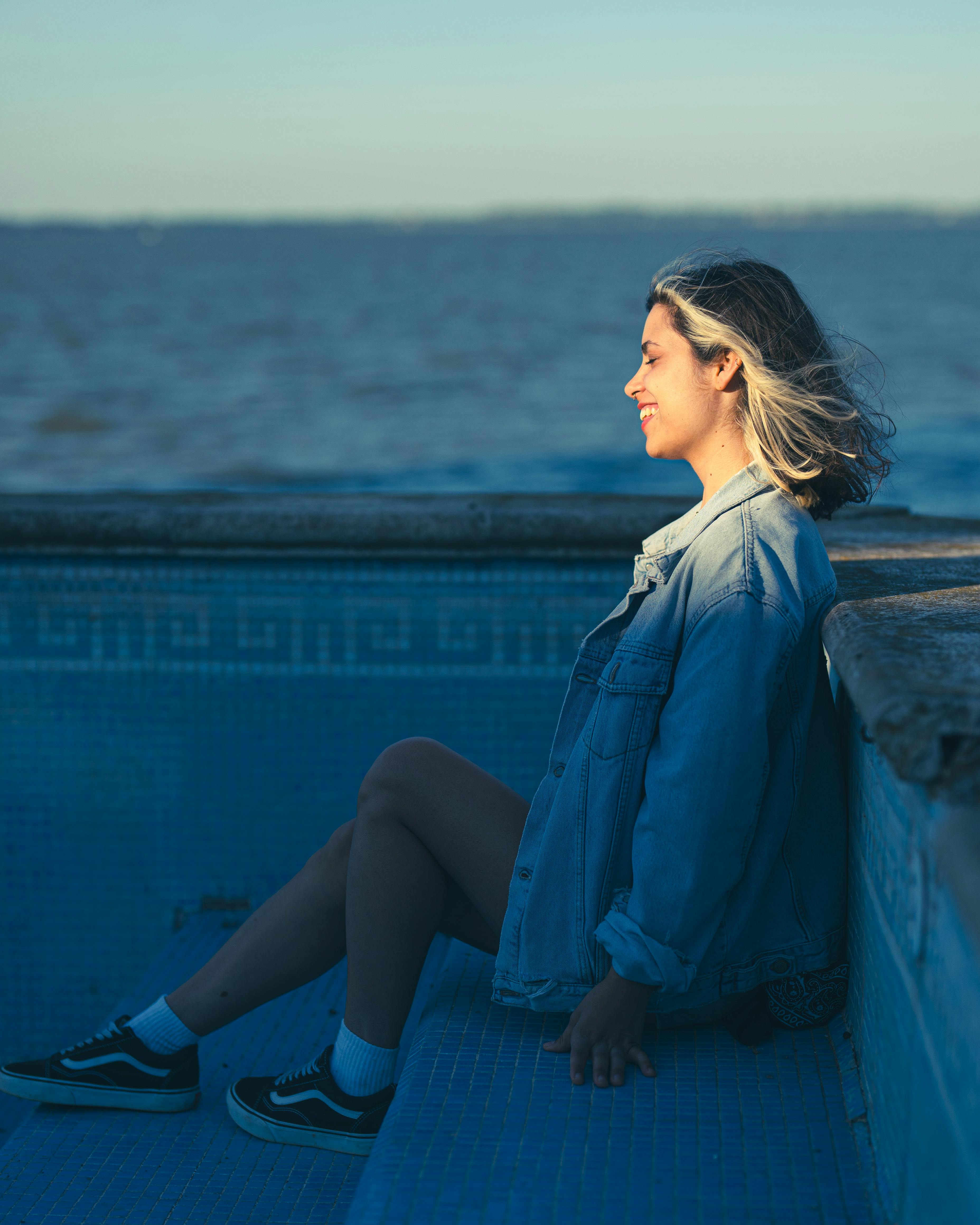 woman in denim jacket sitting by chascomus lake