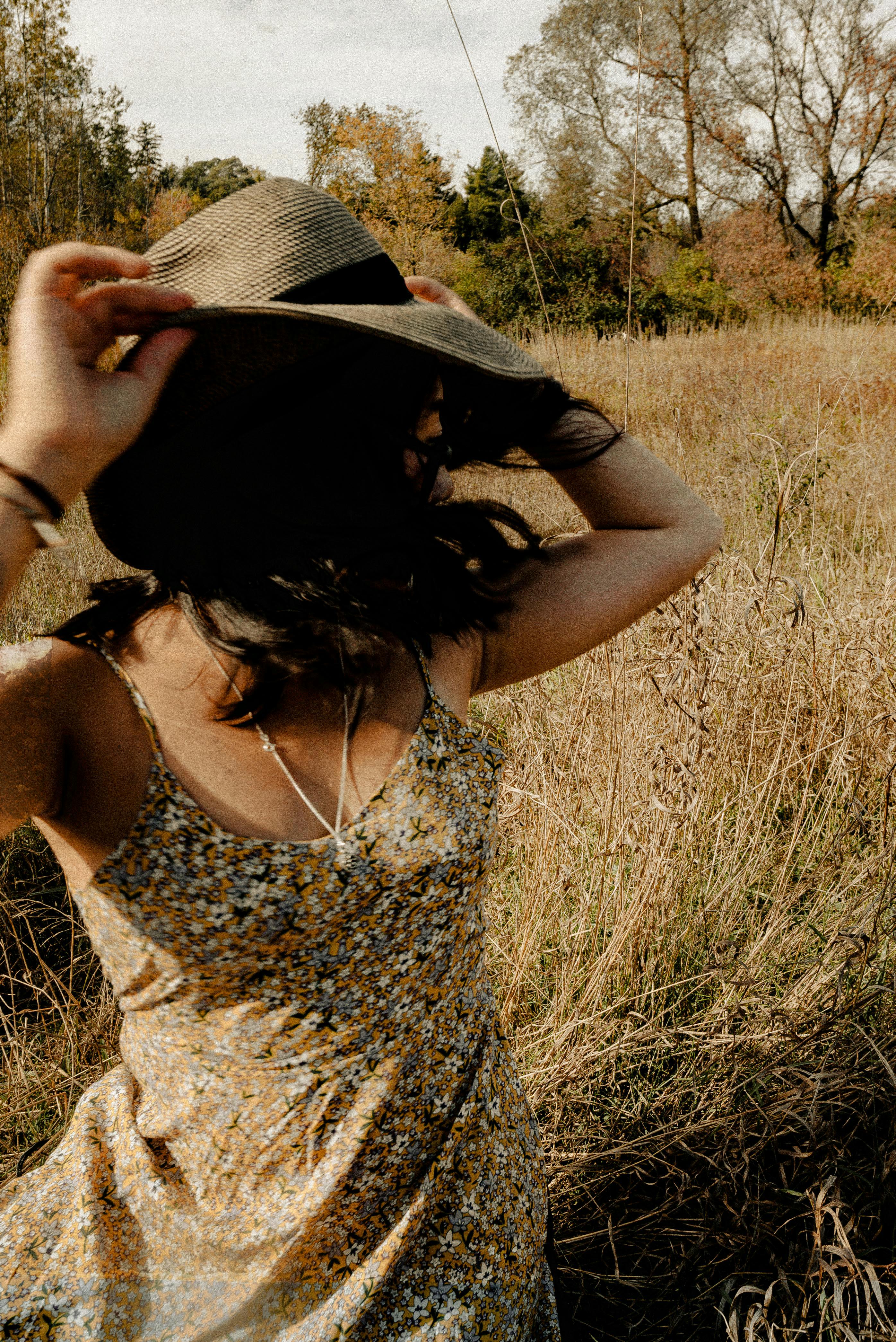 一名妇女穿着花卉连衣裙，戴着遮阳帽，在乡村草地上享受阳光明媚的一天