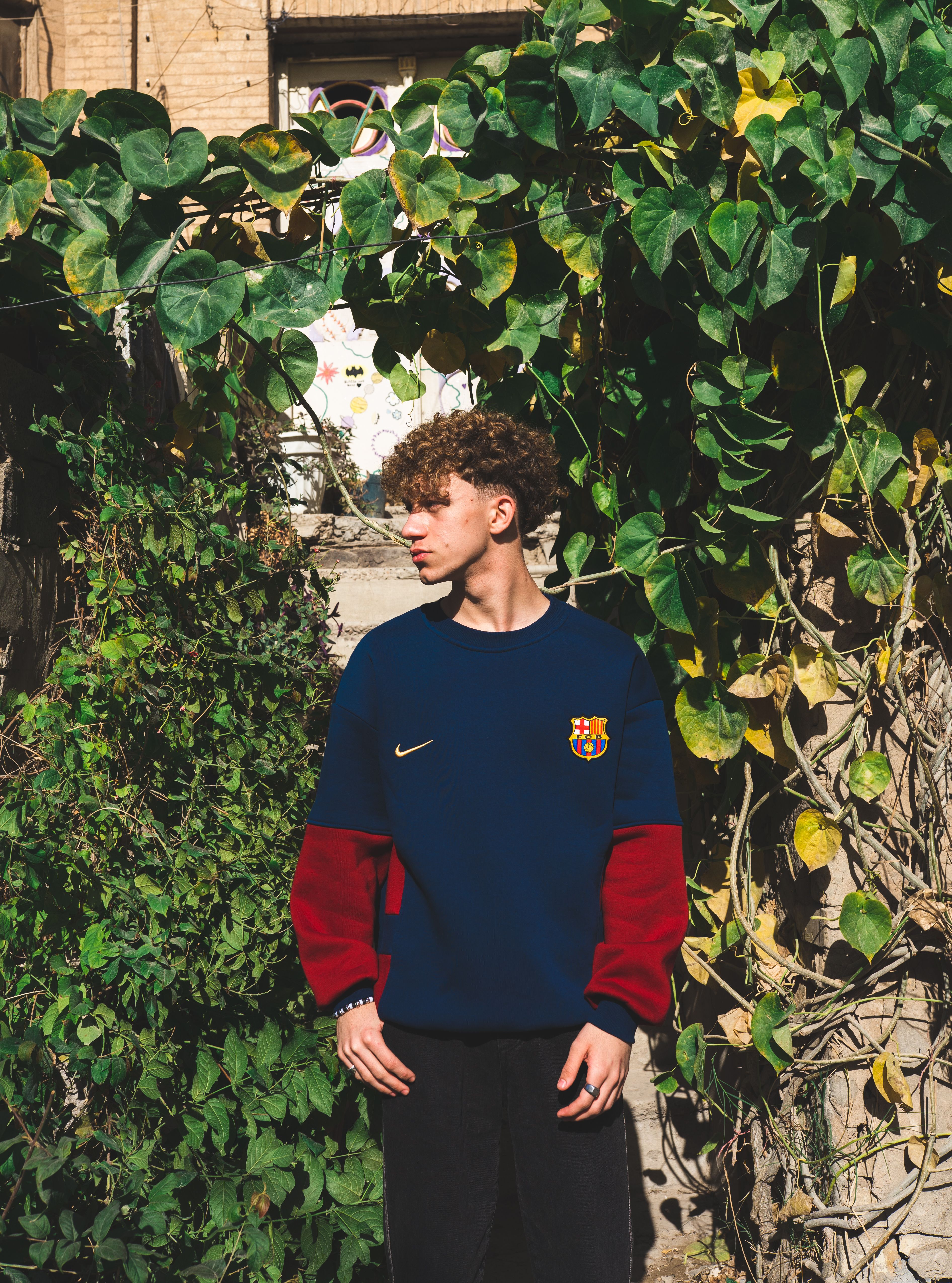 Casual young man in a Barcelona sports jersey stands by lush green ivy.