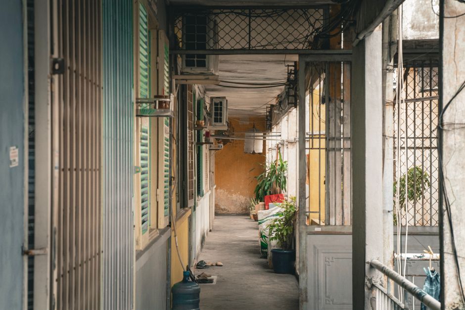 Explore a rustic Vietnamese apartment corridor with vintage shutters and greenery.