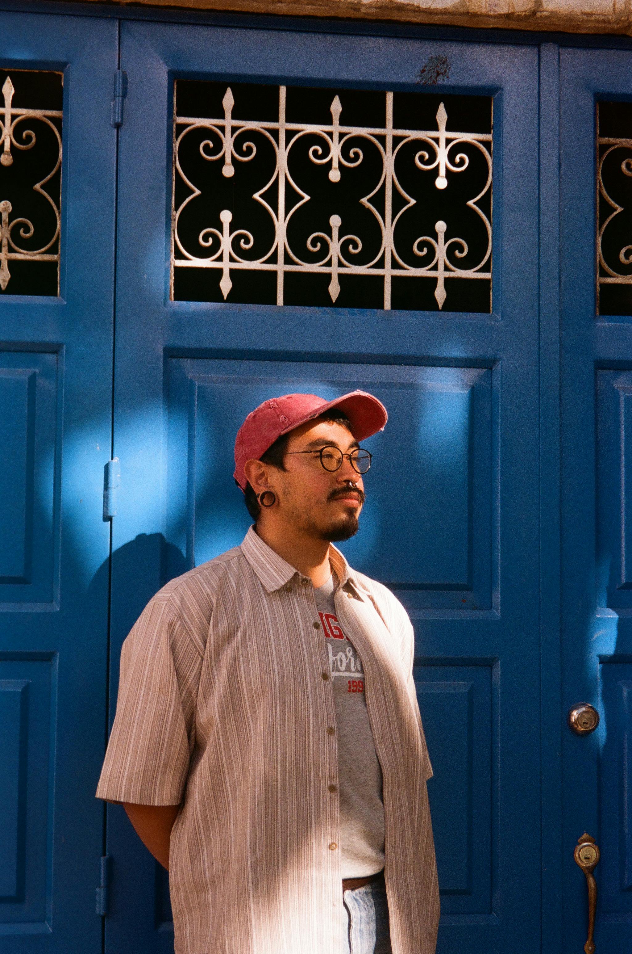 A fashionable young man stands in front of a vibrant blue door, highlighting urban style in Colombia.