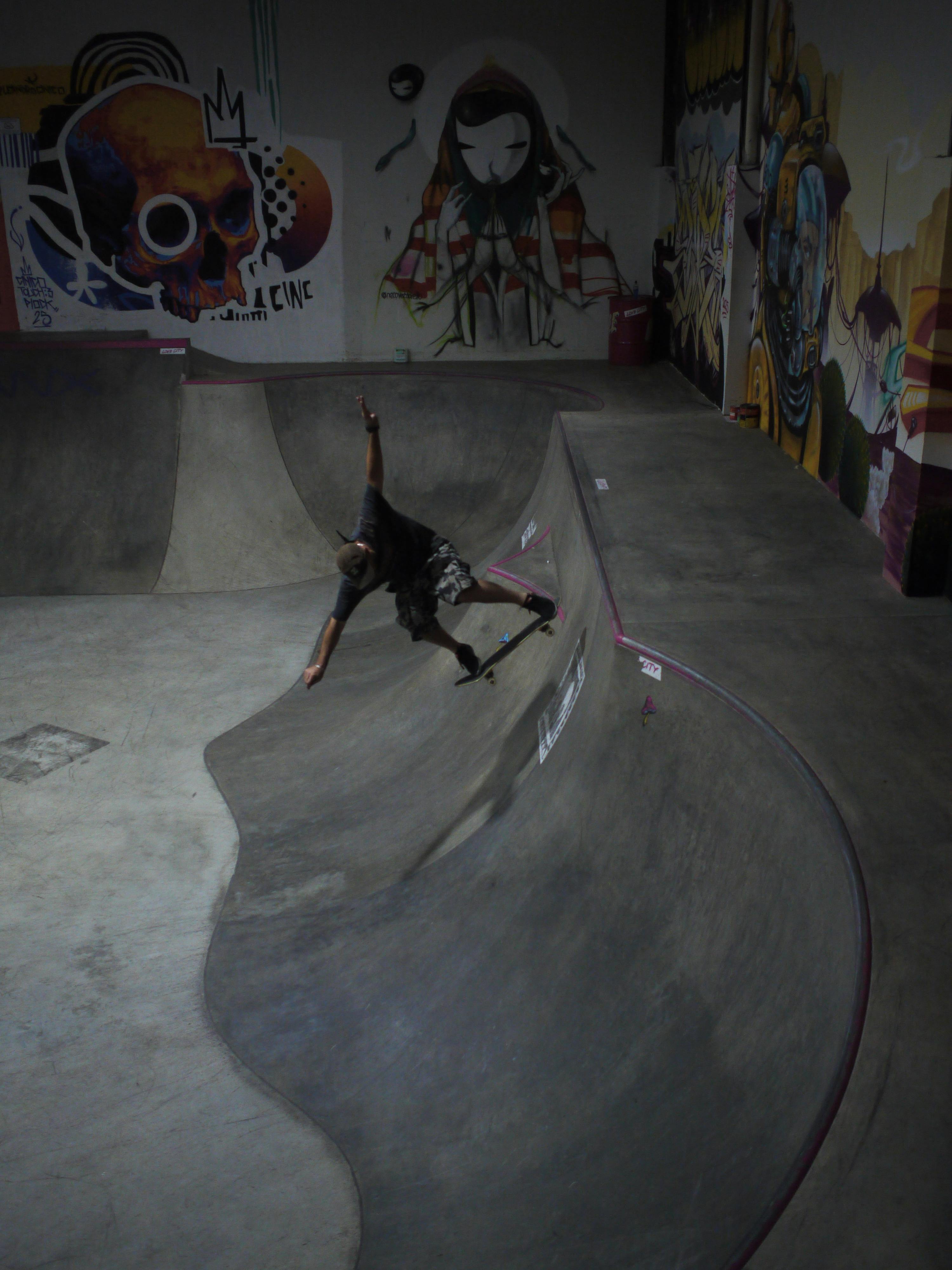 Skateboarder performing tricks in an indoor skatepark in Curitiba, Brazil, showcasing vibrant street art.