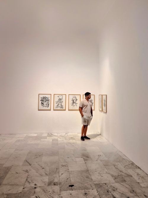 Free A man examines framed artwork on a minimalist gallery wall, creating a thoughtful scene. Stock Photo