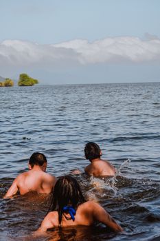 Three children swimming in a tranquil lake under a clear sky.