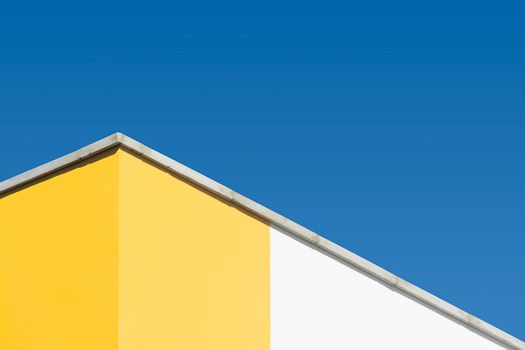 Modern building facade with yellow and white walls under a clear blue sky.