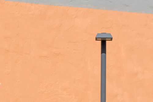 Free A minimalist view of a streetlight against a vibrant orange wall. Perfect for modern design themes. Stock Photo