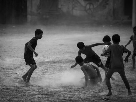 Children engaged in an energetic football game on a dusty outdoor field.
