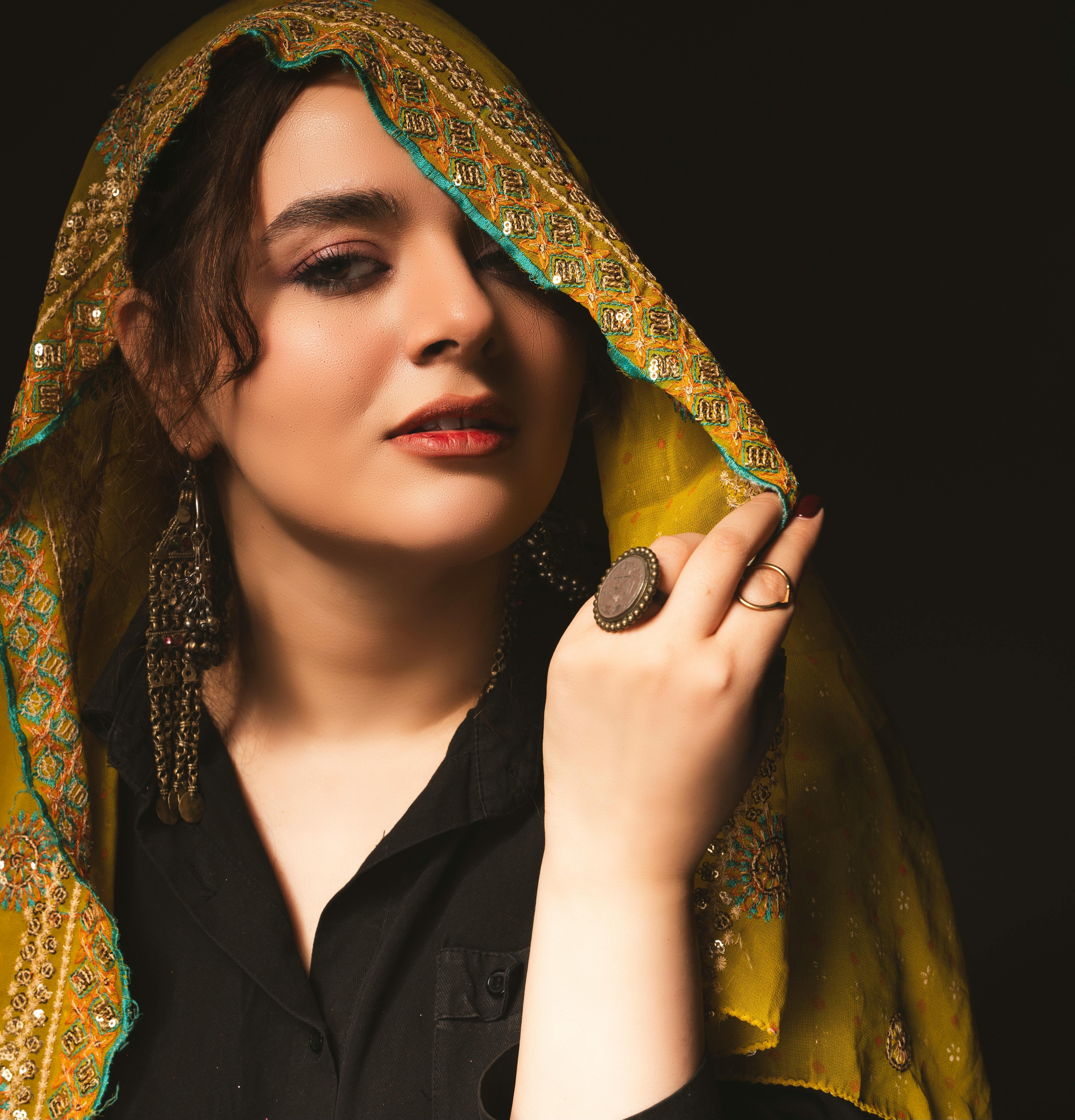 Portrait of a woman in a colorful traditional attire with intricate jewelry against a dark background.