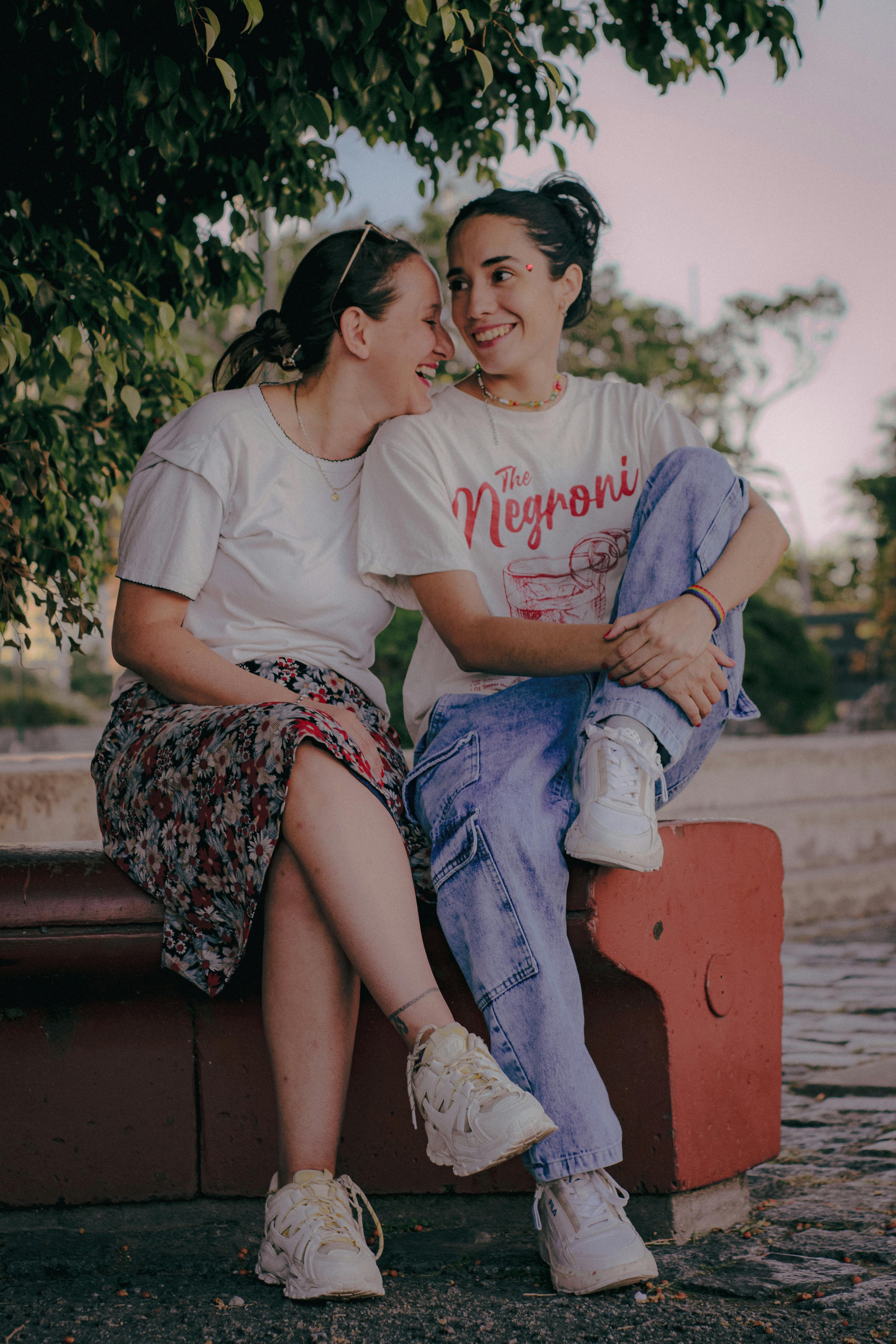 Two young women sitting together, laughing and enjoying a joyful moment outdoors on a bench.