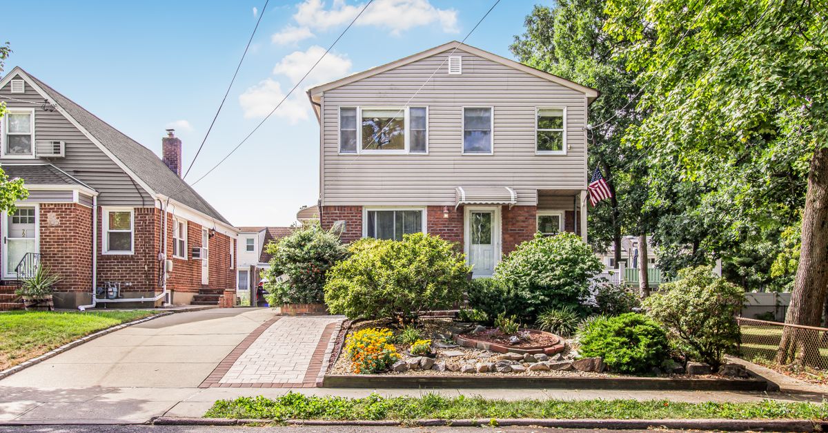 A suburban two-story house with a lush garden on a sunny day.