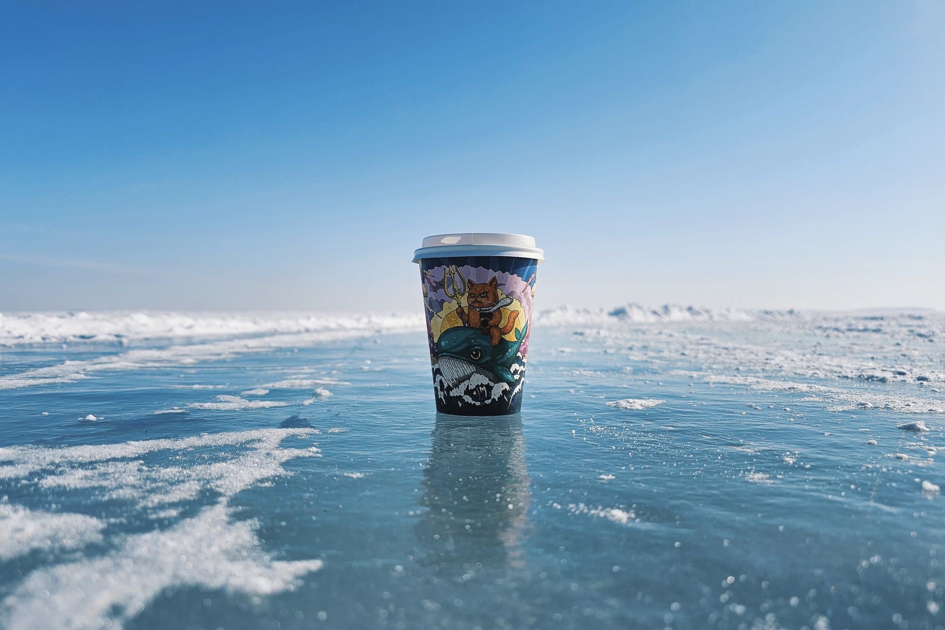 Vibrant coffee cup on icy lake under clear blue sky.
