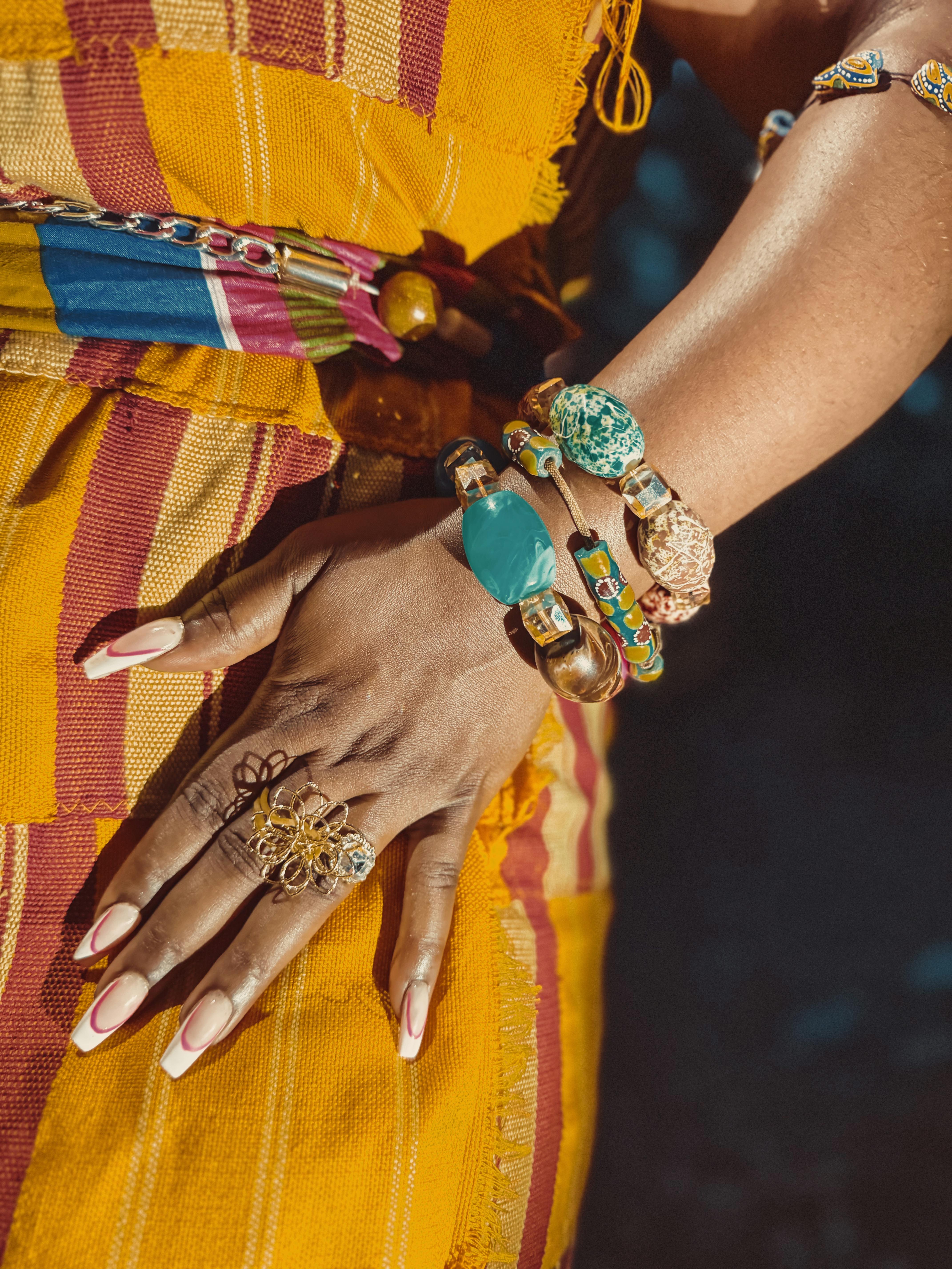 Ücretsiz Gana'da rengarenk bilezikler ve kente kumaşıyla süslenmiş bir kadının elinin yakın çekim fotoğrafı. Stok Fotoğraflar