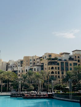 Sunny view of Mediterranean-style buildings and palms reflecting in a tranquil pool.