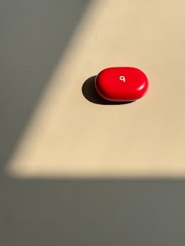 A red earbud case casting a shadow on a flat surface with sunlight.