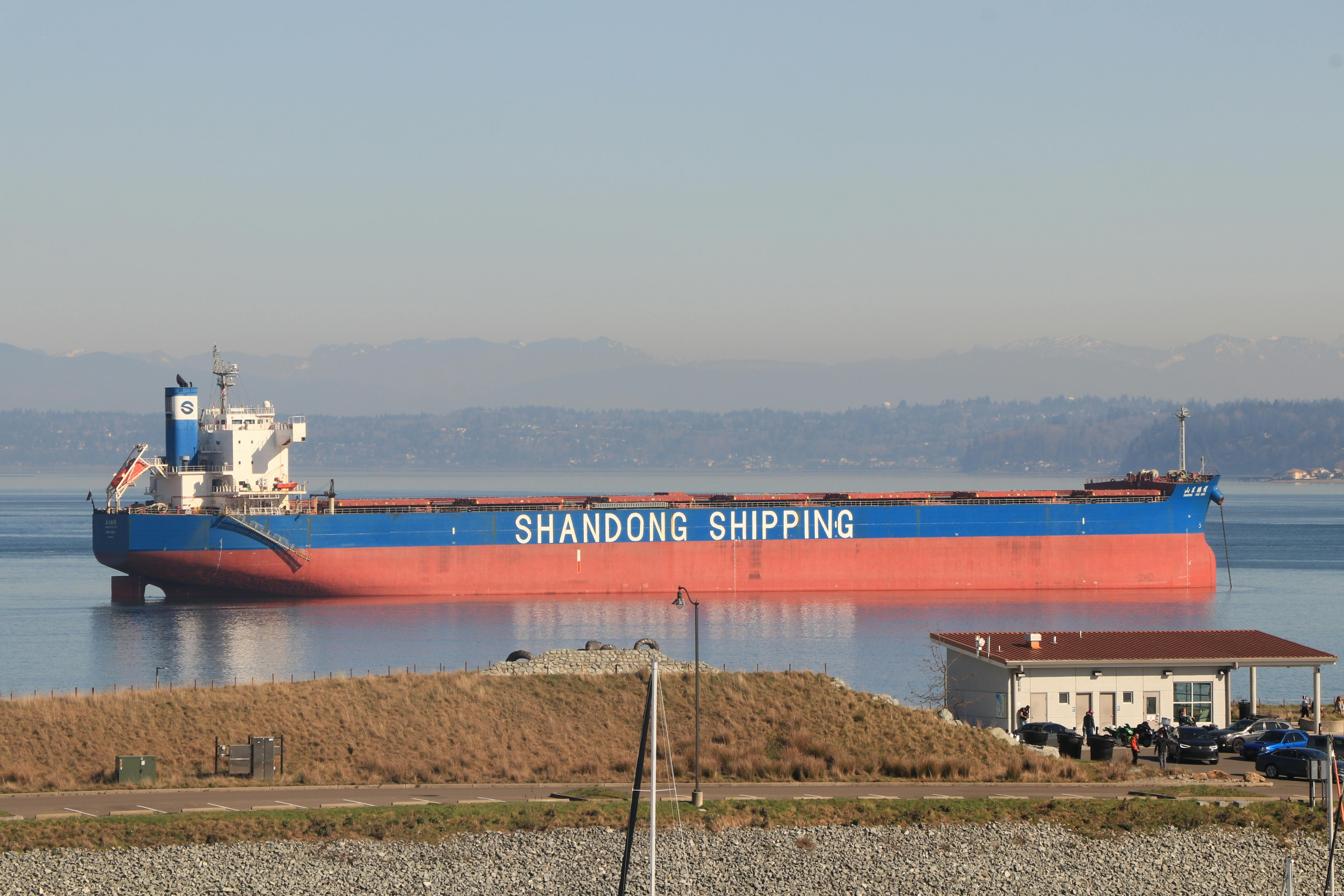 Cargo ship 'Shandong Shipping' docked in Seattle, showcasing serene waters and mountain backdrop.