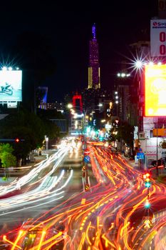 Long exposure captures colorful night traffic through a bustling city with illuminated skyscraper.