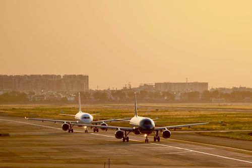 Free Two commercial airplanes taxiing at sunset with cityscape in background. Stock Photo