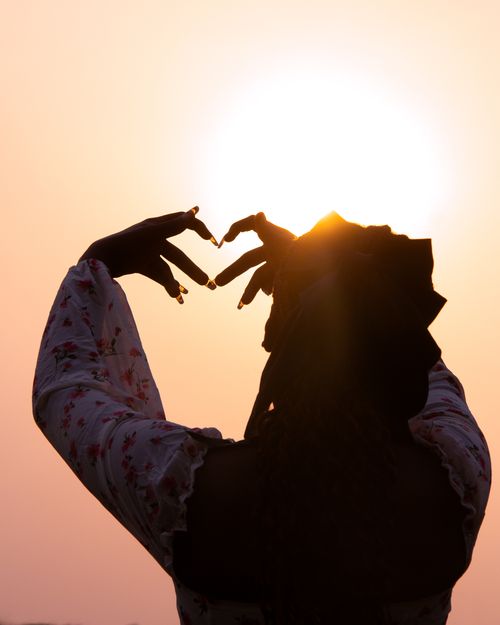 Free A woman forms a heart shape with her hands against a glowing sunset sky. Stock Photo