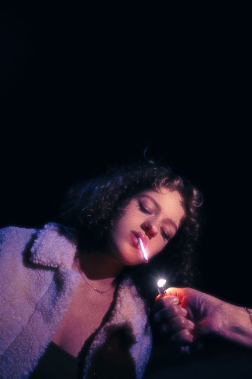 Free Young woman in cozy jacket lighting a cigarette outdoors at night, showcasing a moody atmosphere. Stock Photo