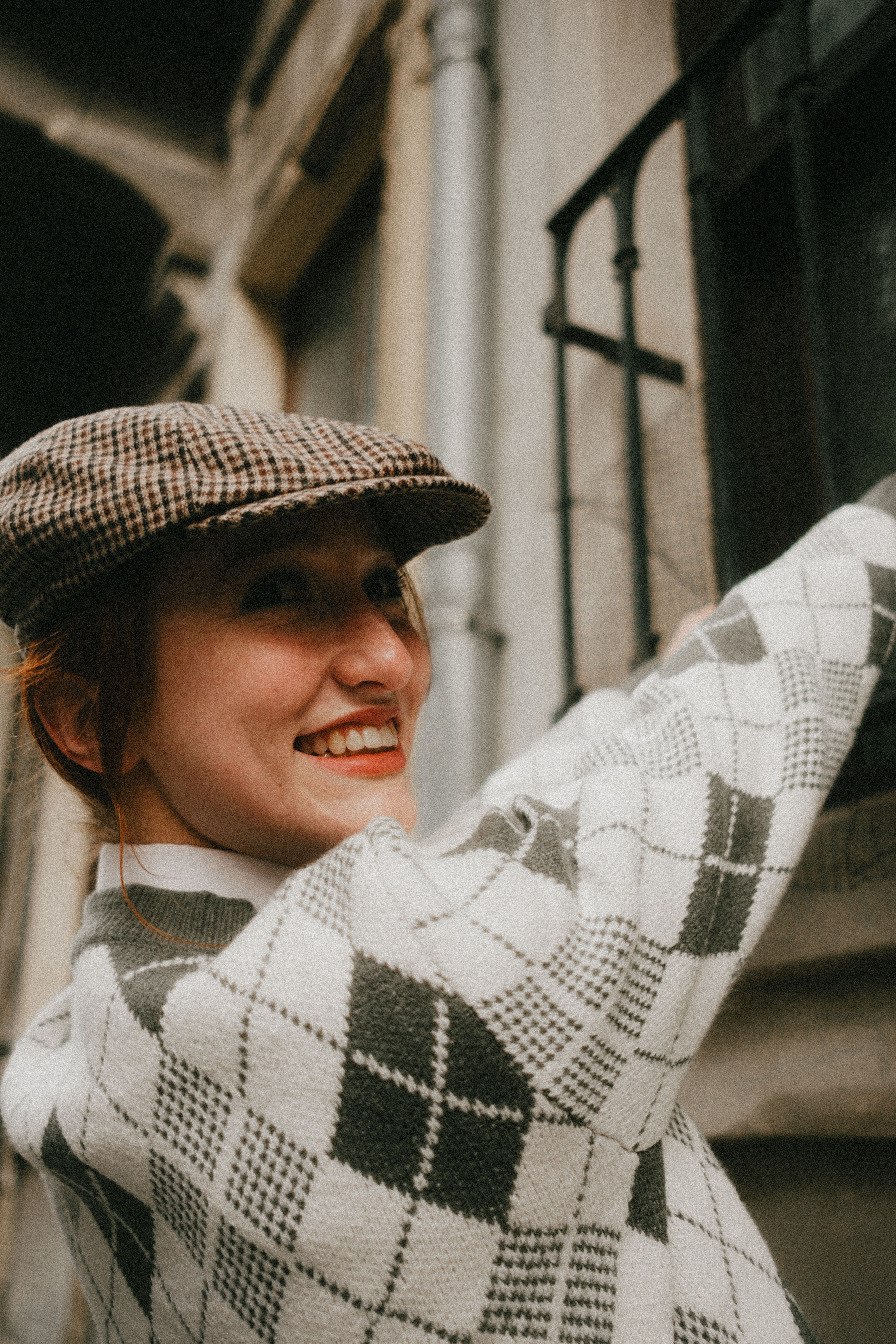 Bright smile captured as woman in vintage sweater reaches upwards in urban setting.