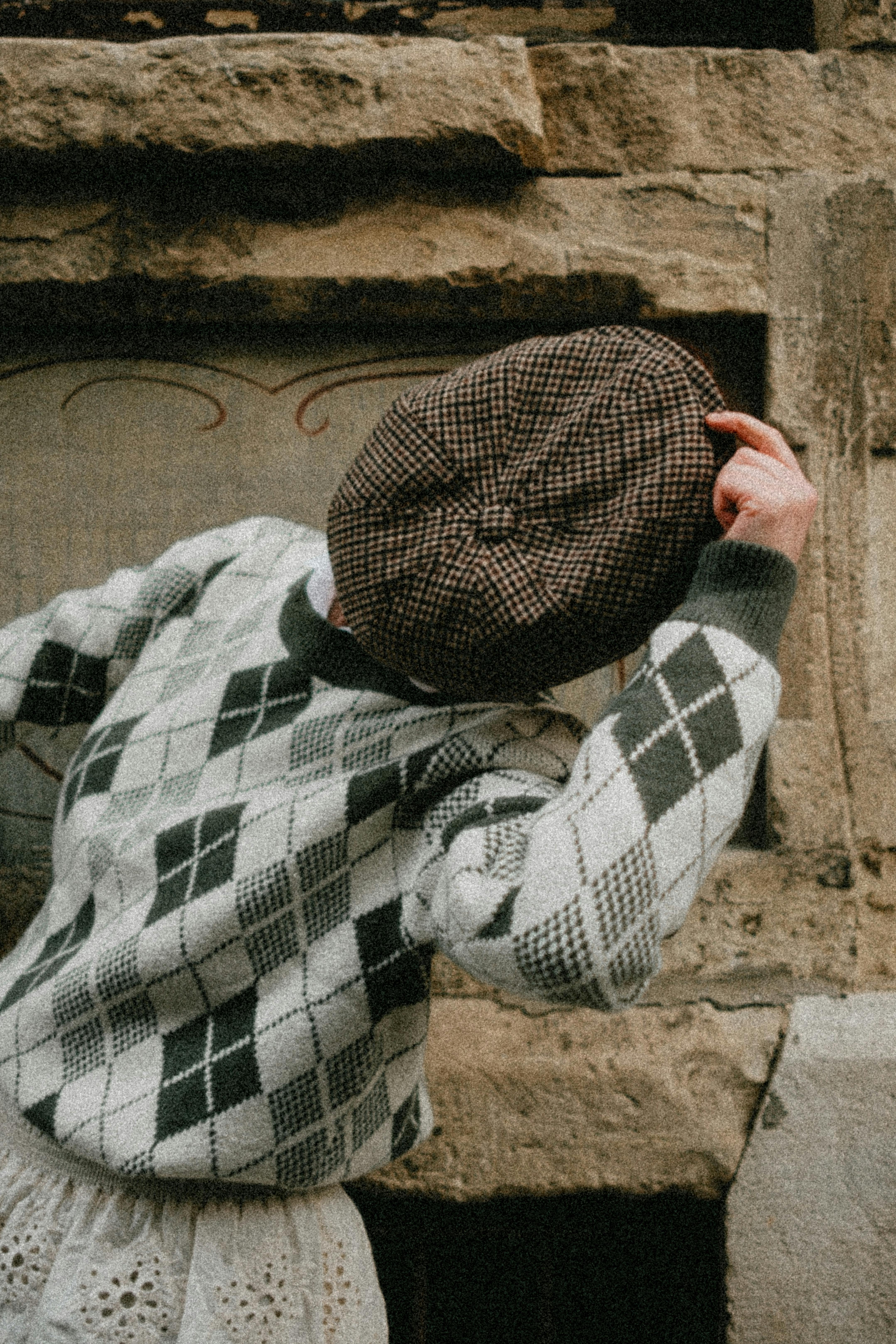 Stylish person in vintage clothing strikes a pose outdoors against stone wall.