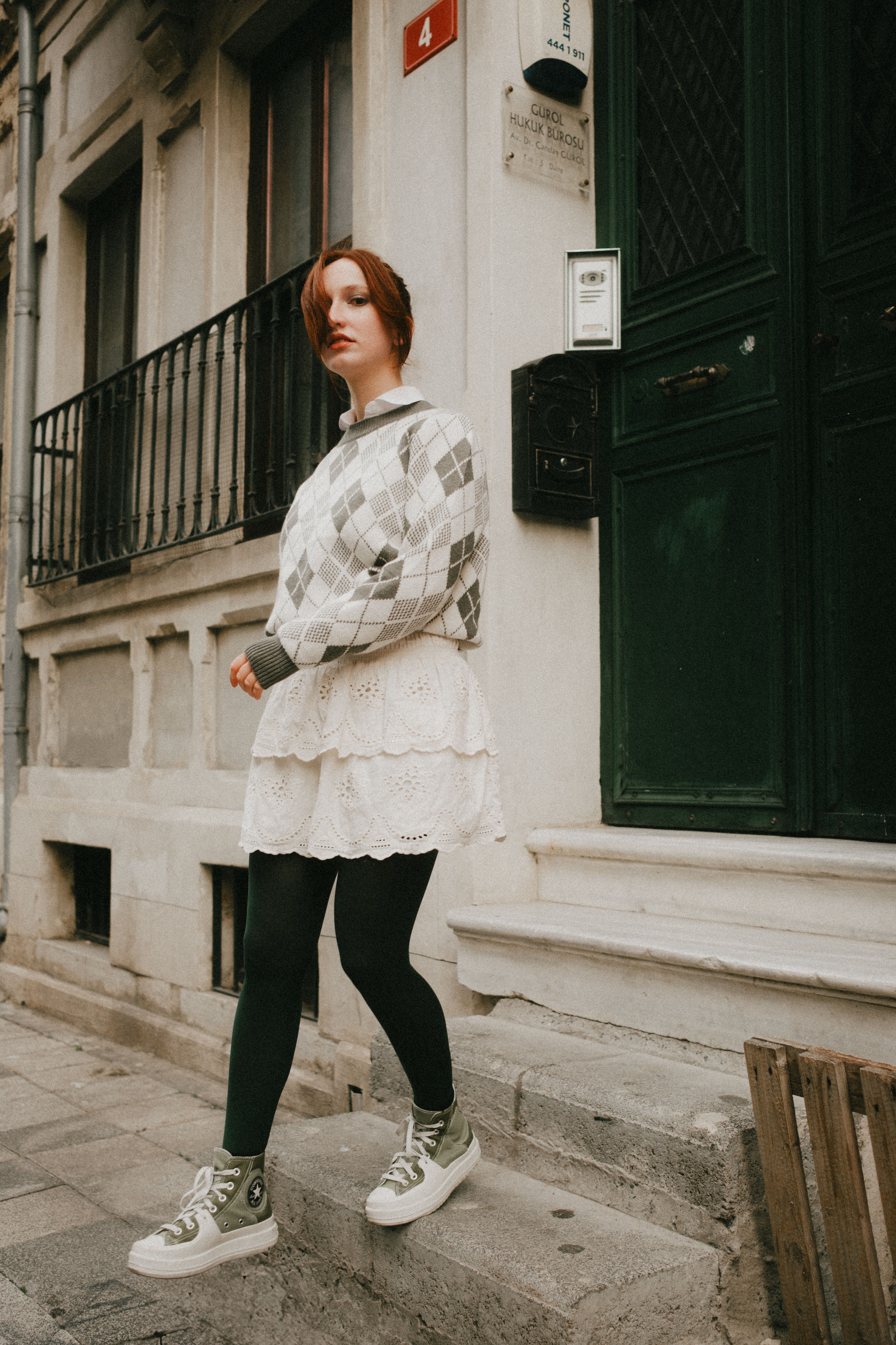 Stylish woman in an argyle sweater poses in a city street setting.