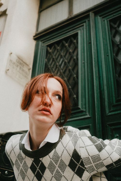 Free Young woman in argyle sweater poses outdoors against a vintage door. Stock Photo
