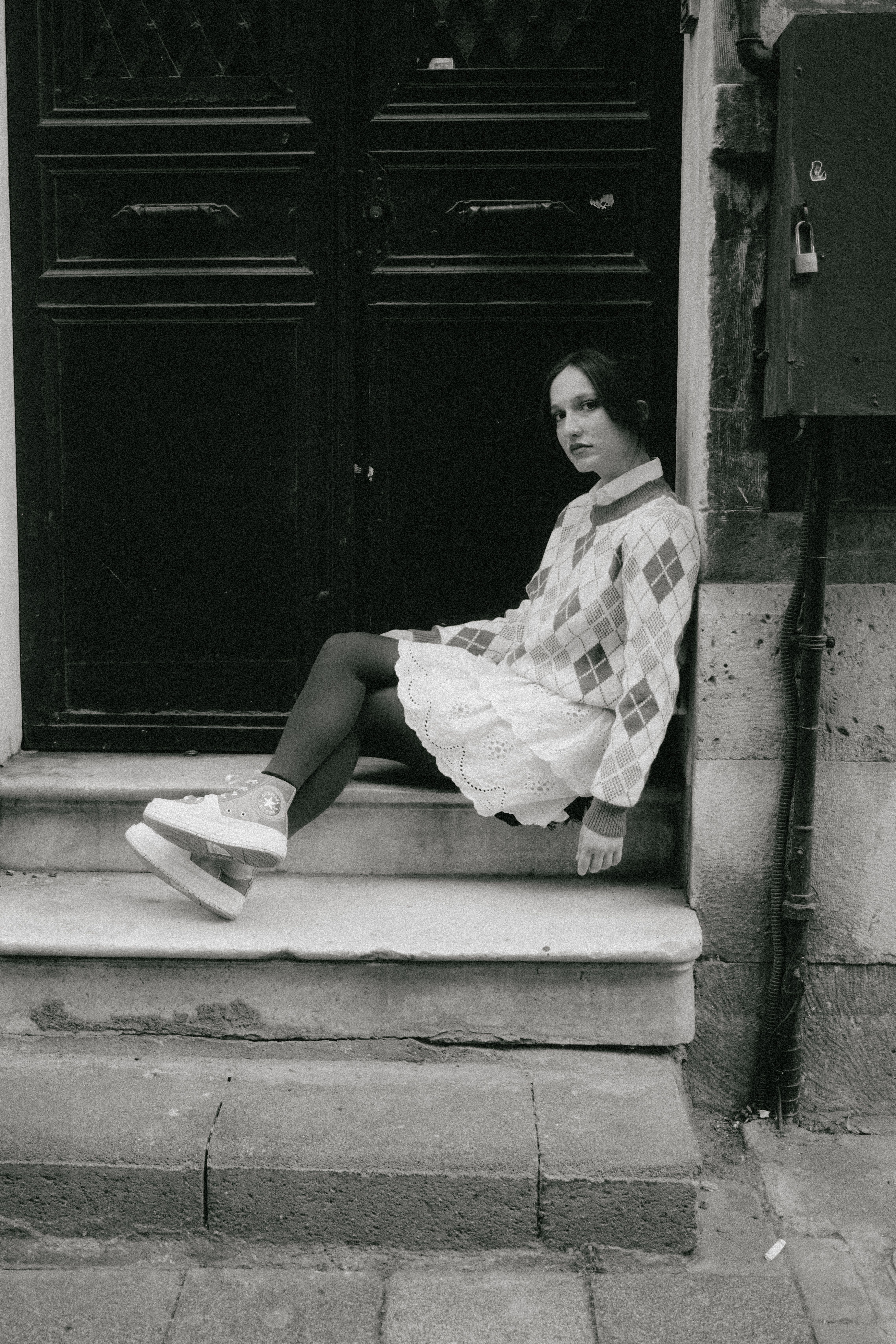 A woman in vintage clothing sits on stone steps in an urban setting.