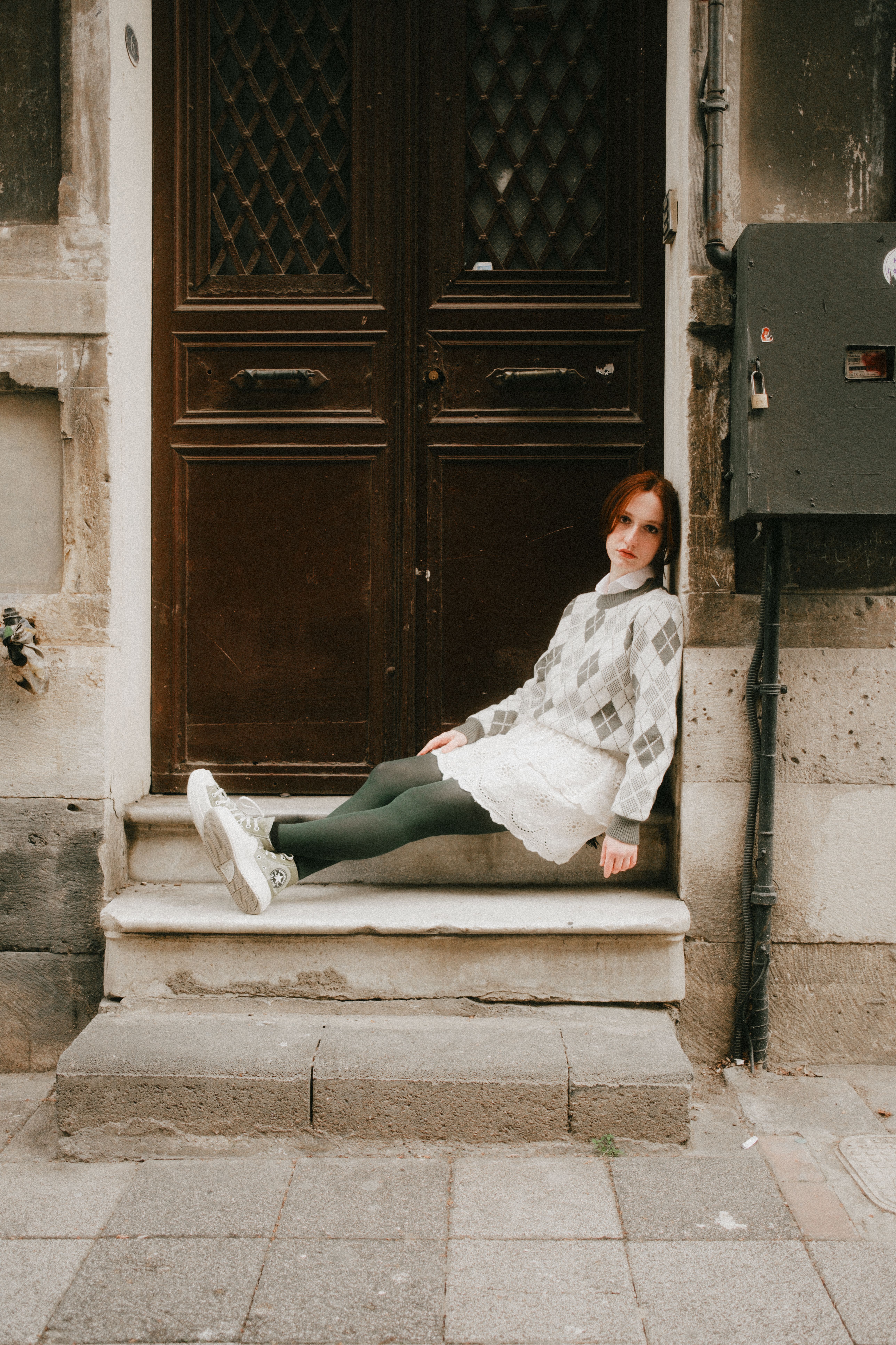 Young woman in a plaid sweater sitting on urban steps, relaxed vibe.