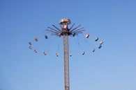 A vertical swing ride reaching high into a clear blue sky at an amusement park.