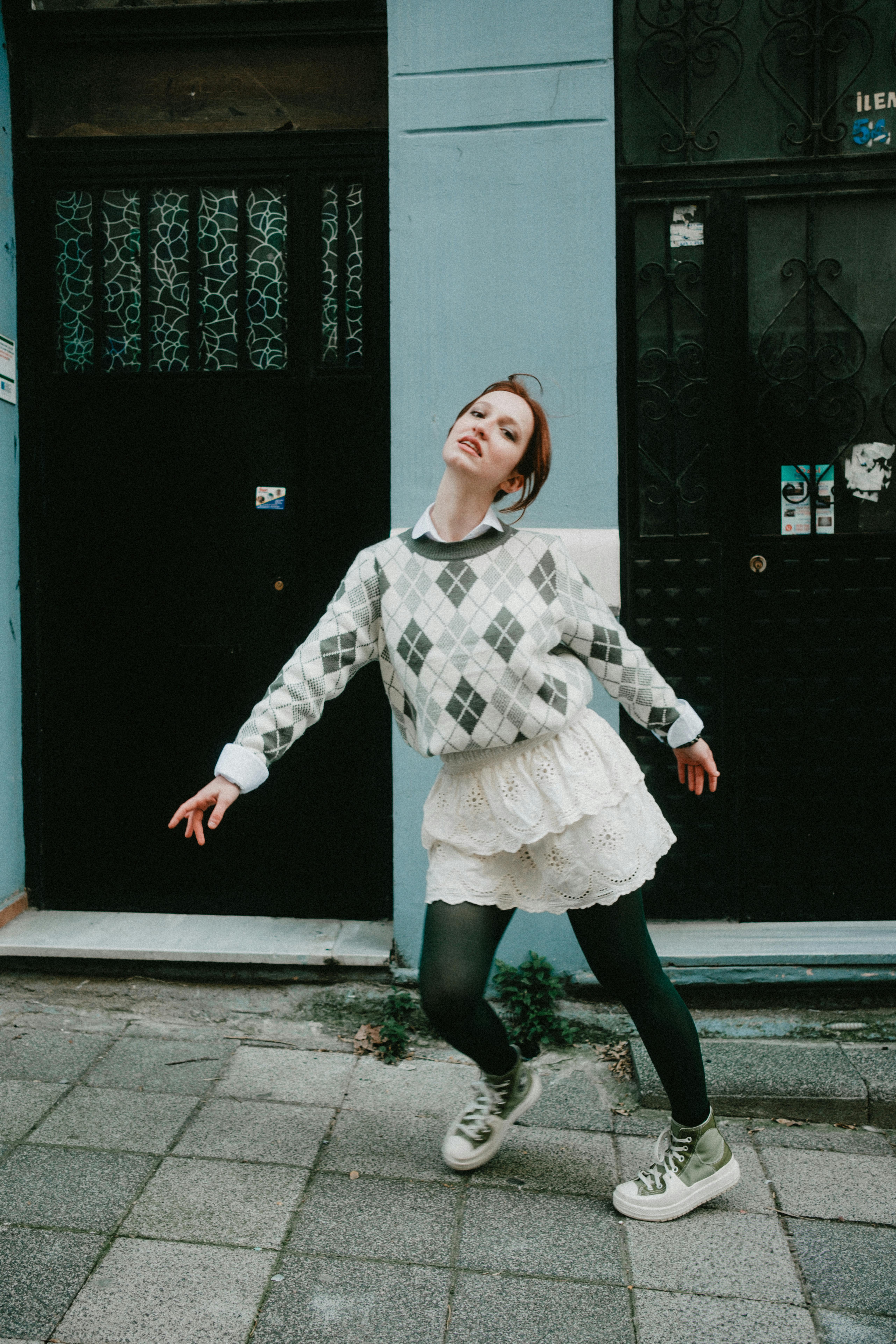 Woman in stylish outfit striking a joyful pose outdoors against blue walls.