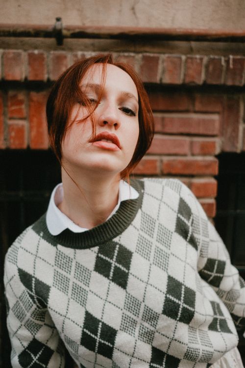 Free Young woman posing confidently in a fashionable argyle sweater outdoors. Stock Photo