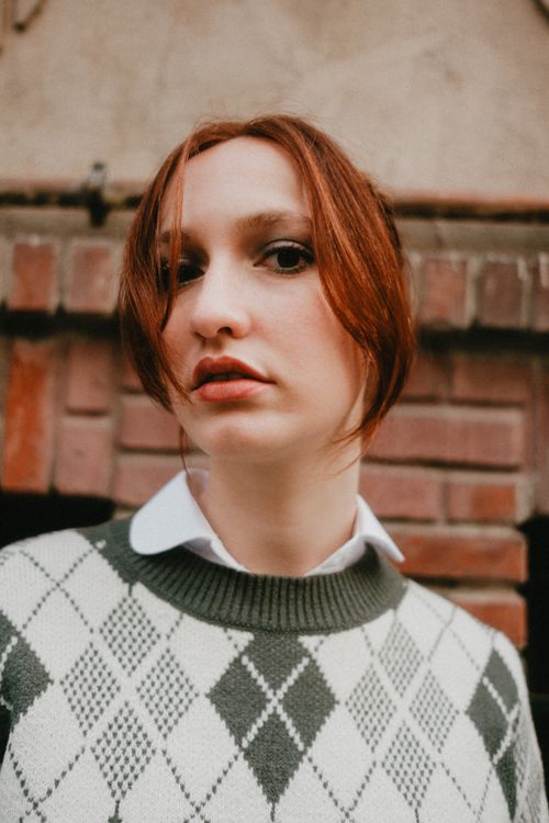 Free Close-up portrait of a woman wearing an argyle sweater, set against a brick wall backdrop. Stock Photo