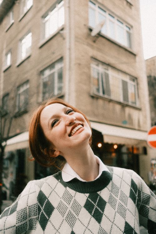 Free Smiling woman in a sweater stands joyfully in a lively urban street. Stock Photo